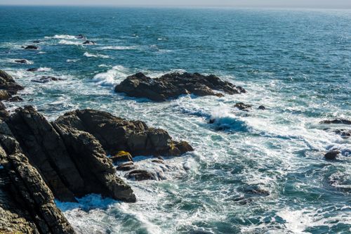 Free Waves crash against rocky coastline on a clear day, capturing the raw power of nature. Stock Photo