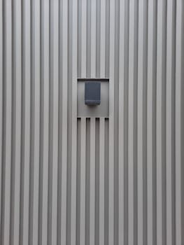 Minimalist design of a gray metal wall featuring a central speaker, creating an industrial aesthetic.
