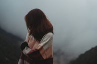 雾蒙蒙的山间，一名穿着针织衫的女子独自站着，享受着宁静
