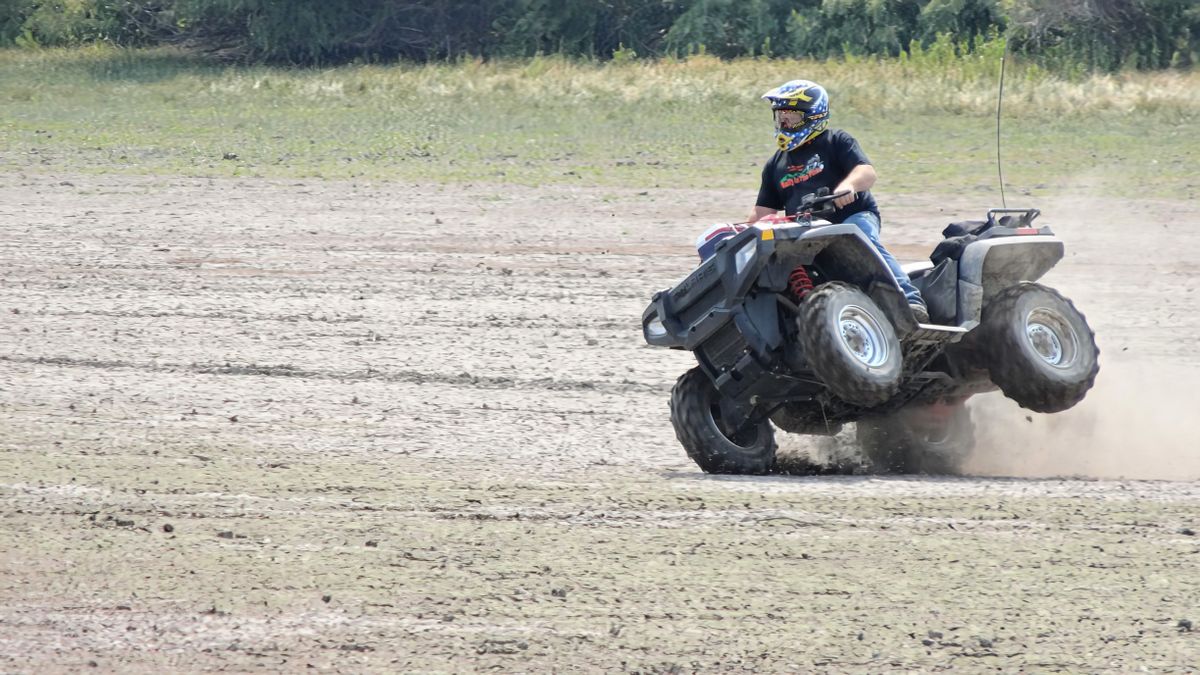 ATV rider wearing helmet and goggles kicking up dust on dirt trail while riding quad off-road