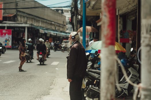 An elderly man with headphones stands on a busy street in Dalat, Vietnam.