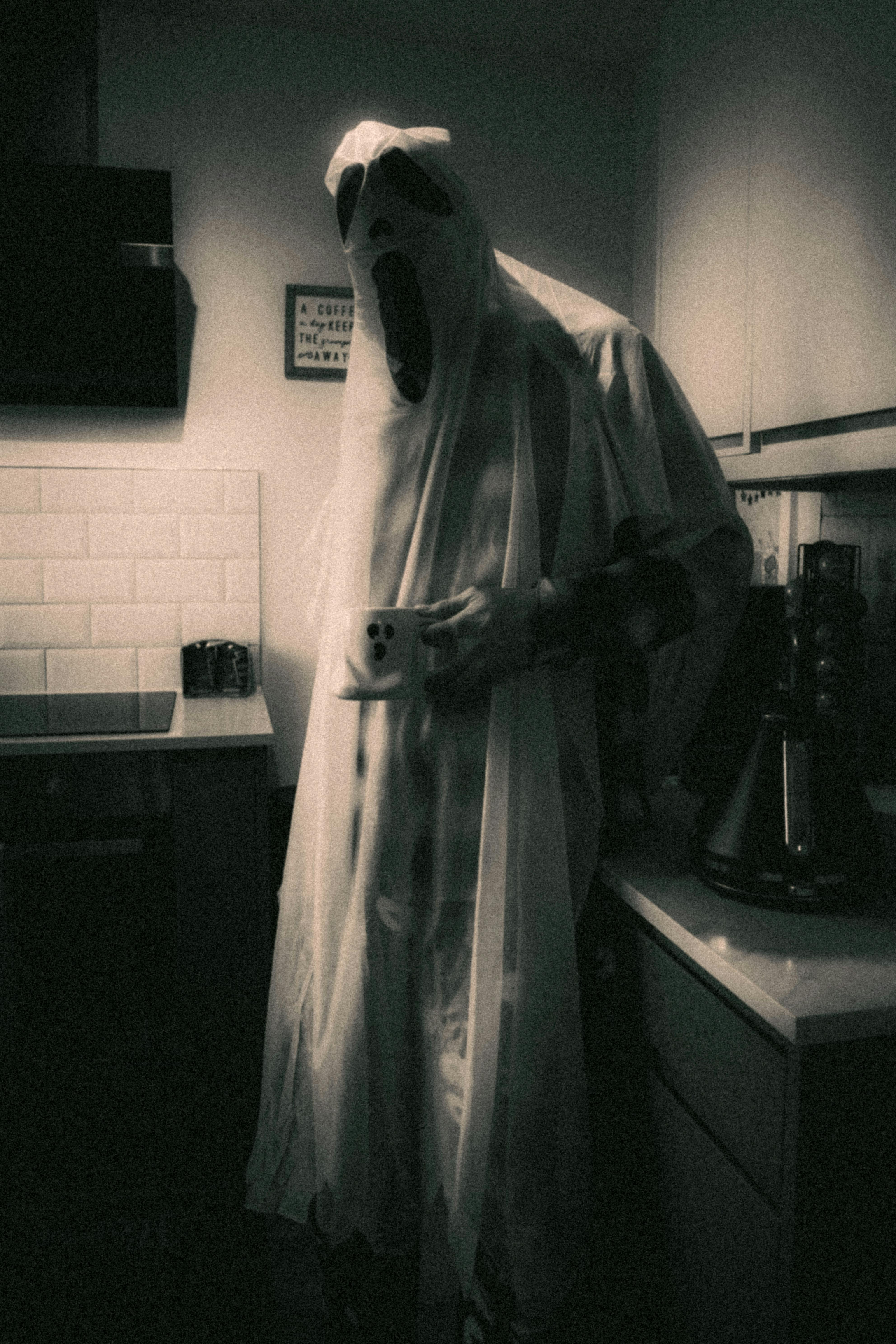Eerie black and white photo of a ghost costume in a kitchen at night.