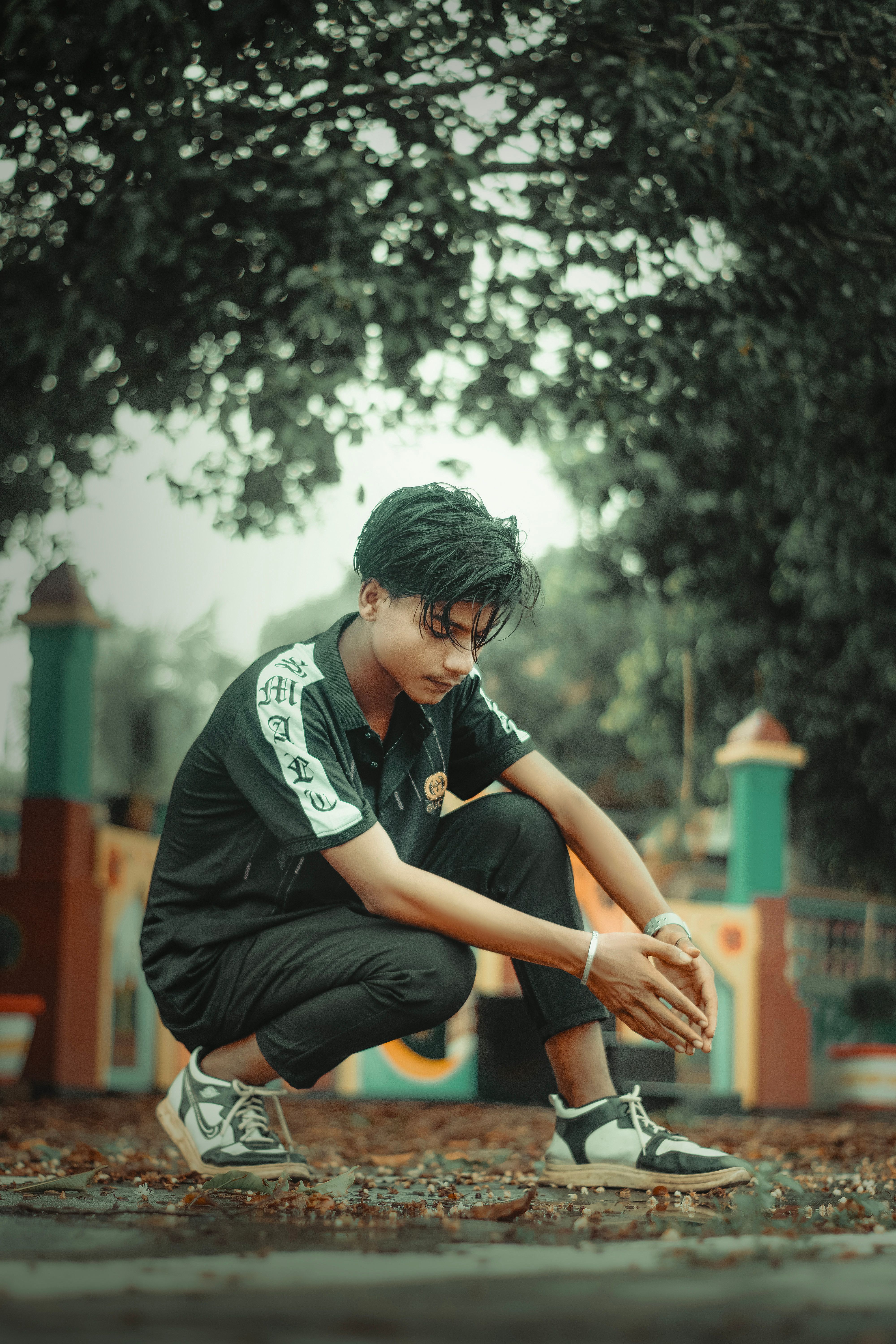 Portrait of a young man crouching outdoors, reflecting in a tranquil village setting.