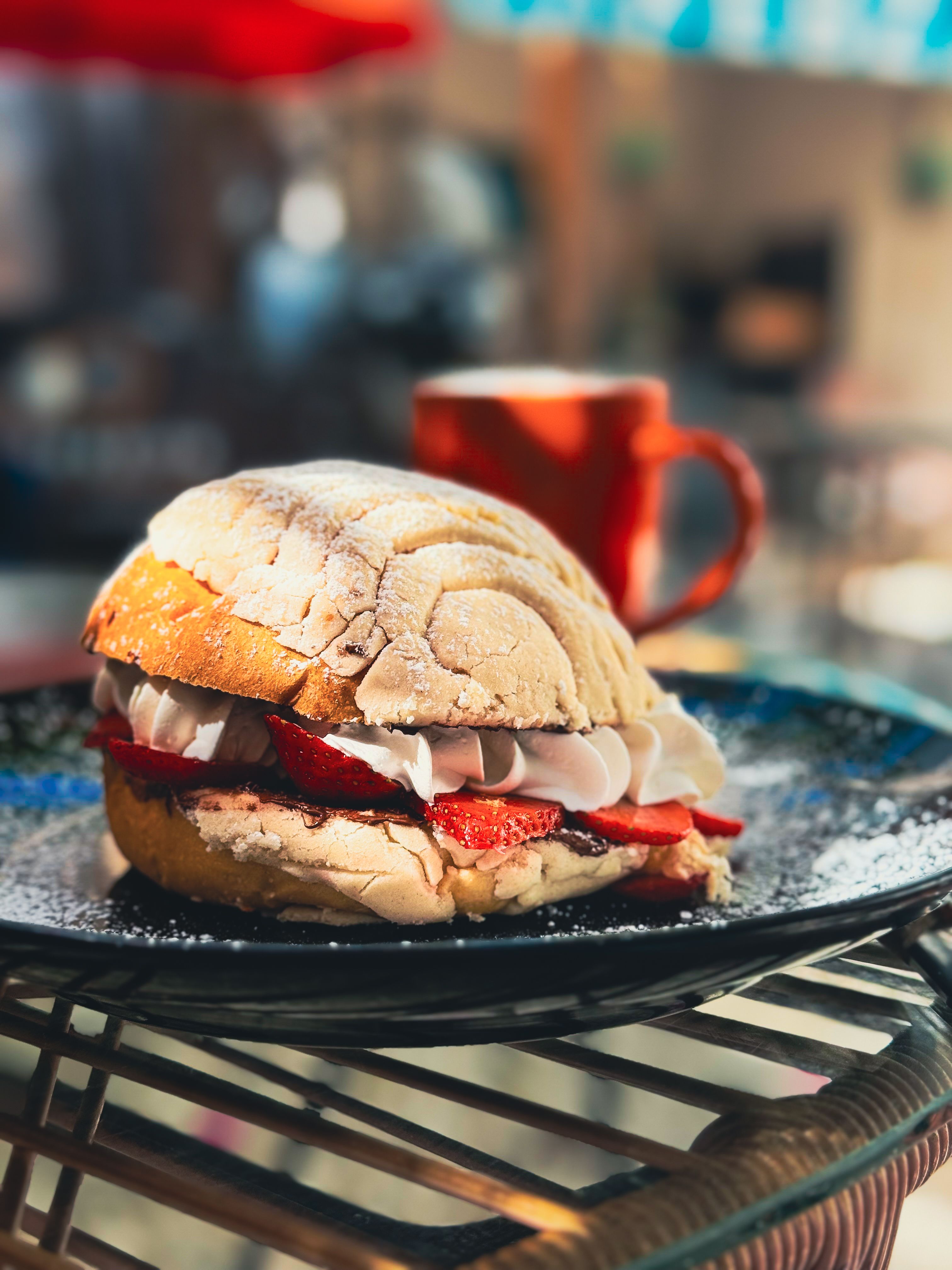 A mouth-watering strawberry concha served on a stylish plate with a coffee in the background, perfect for a sweet break.