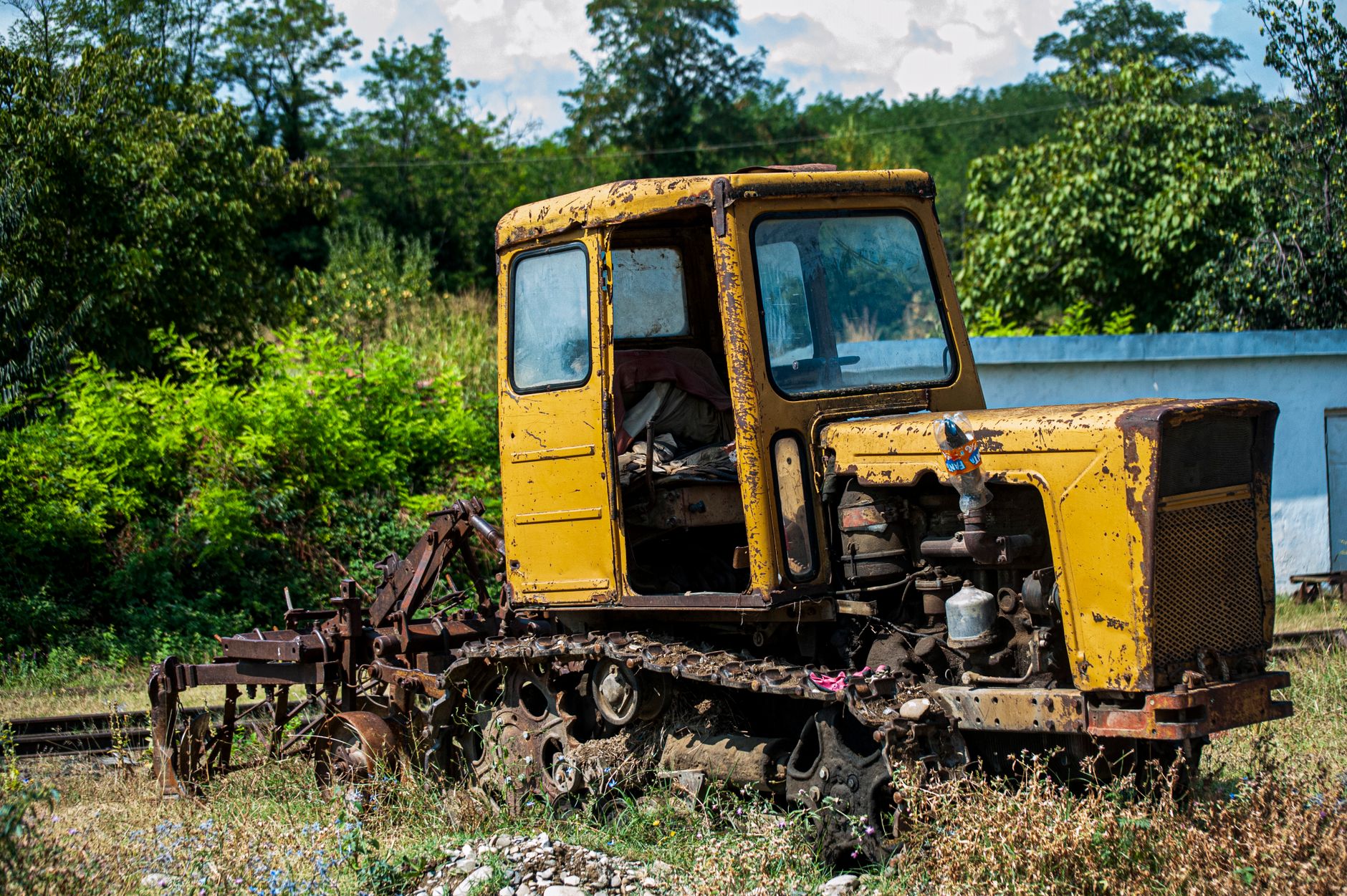 An old, rusty yellow tractor sits abandoned outdoors surrounded by greenery.