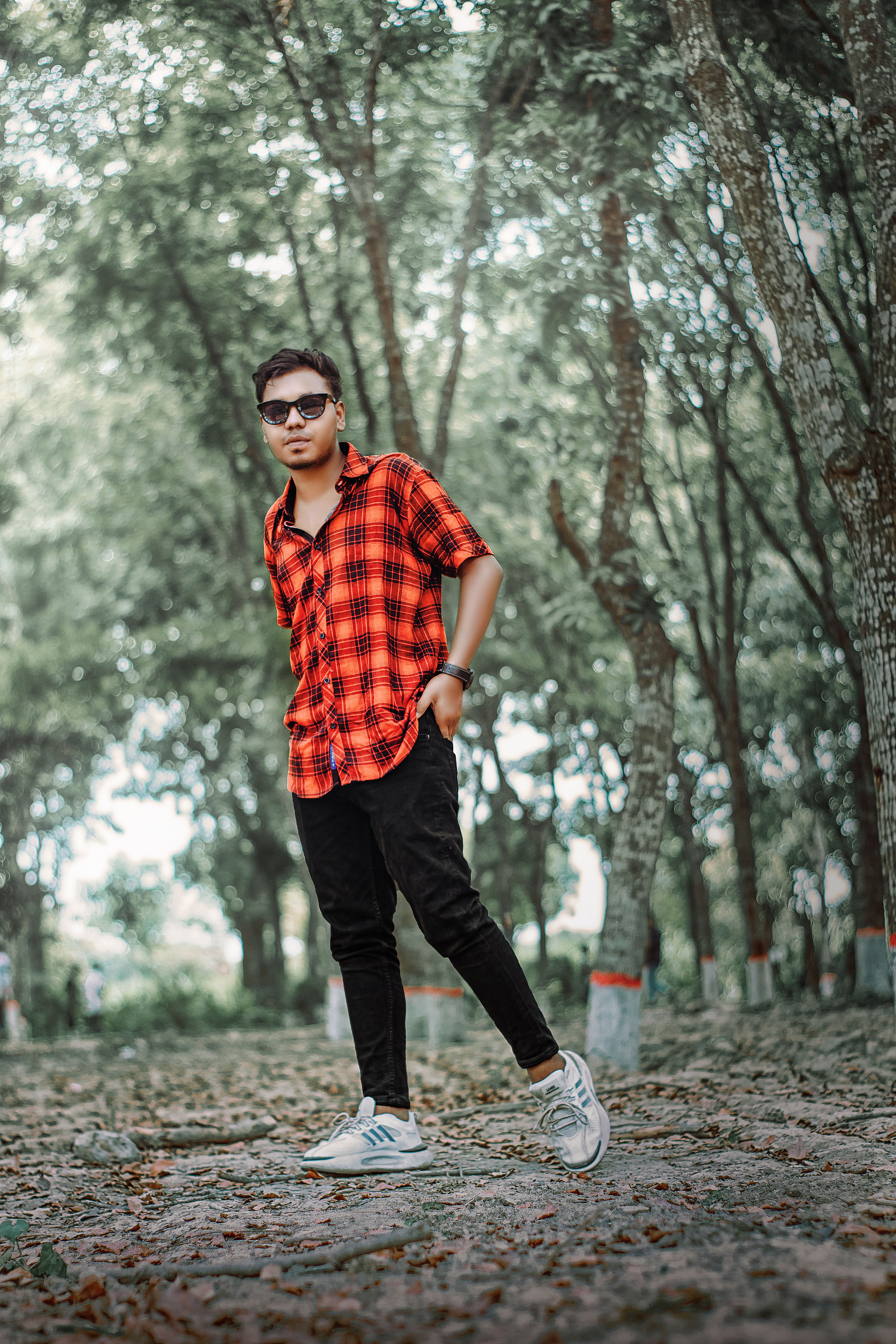 Confident young man in sunglasses poses stylishly in a lush forest setting.