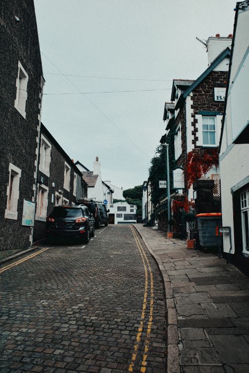 Free Scenic cobblestone street in Conwy, Wales, lined with historic buildings under a cloudy sky. Stock Photo