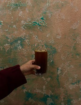 Hand holding glass of iced coffee against a decorative wall in Istanbul.