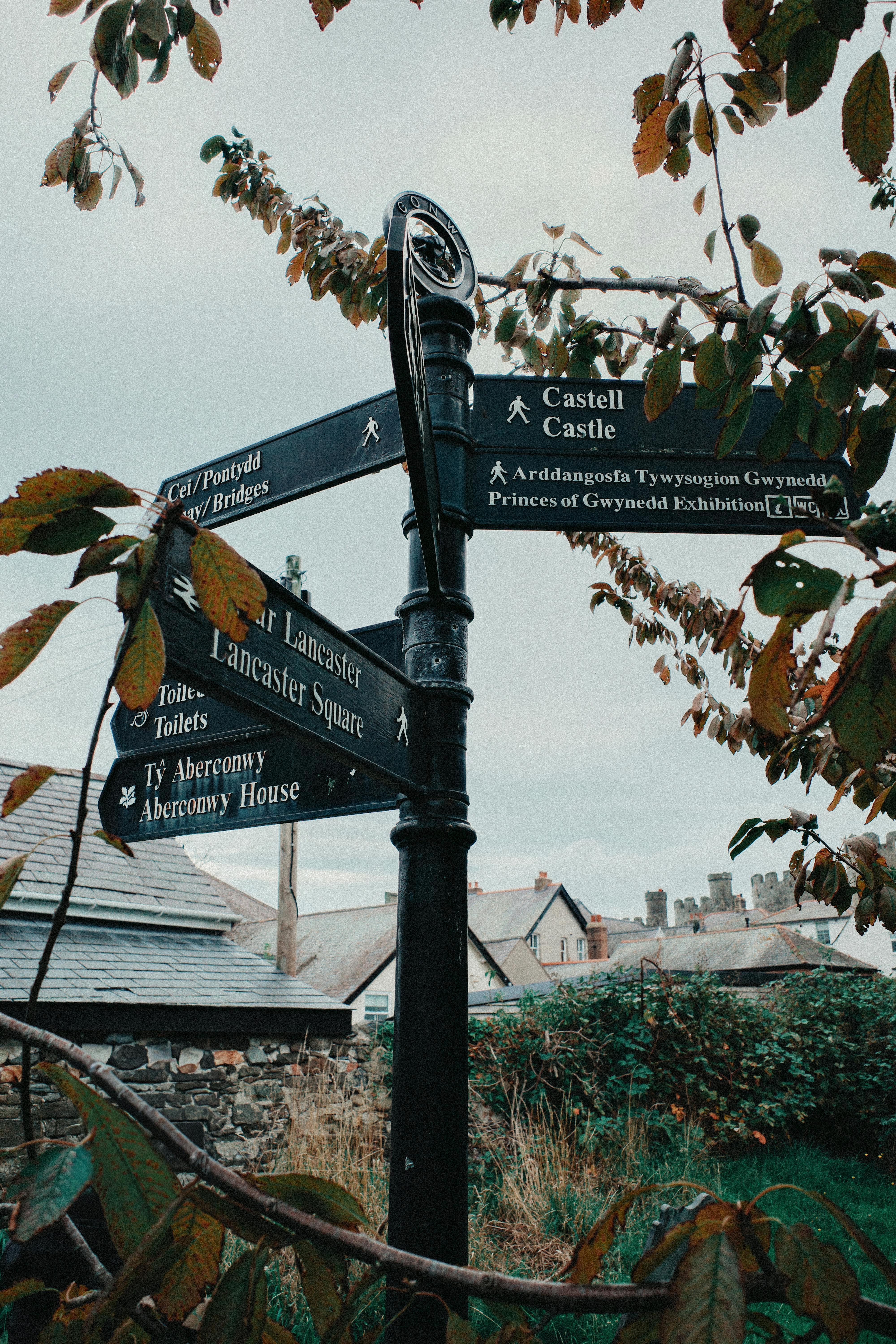 A rustic signpost in Conwy, Wales, guiding visitors to local attractions.
