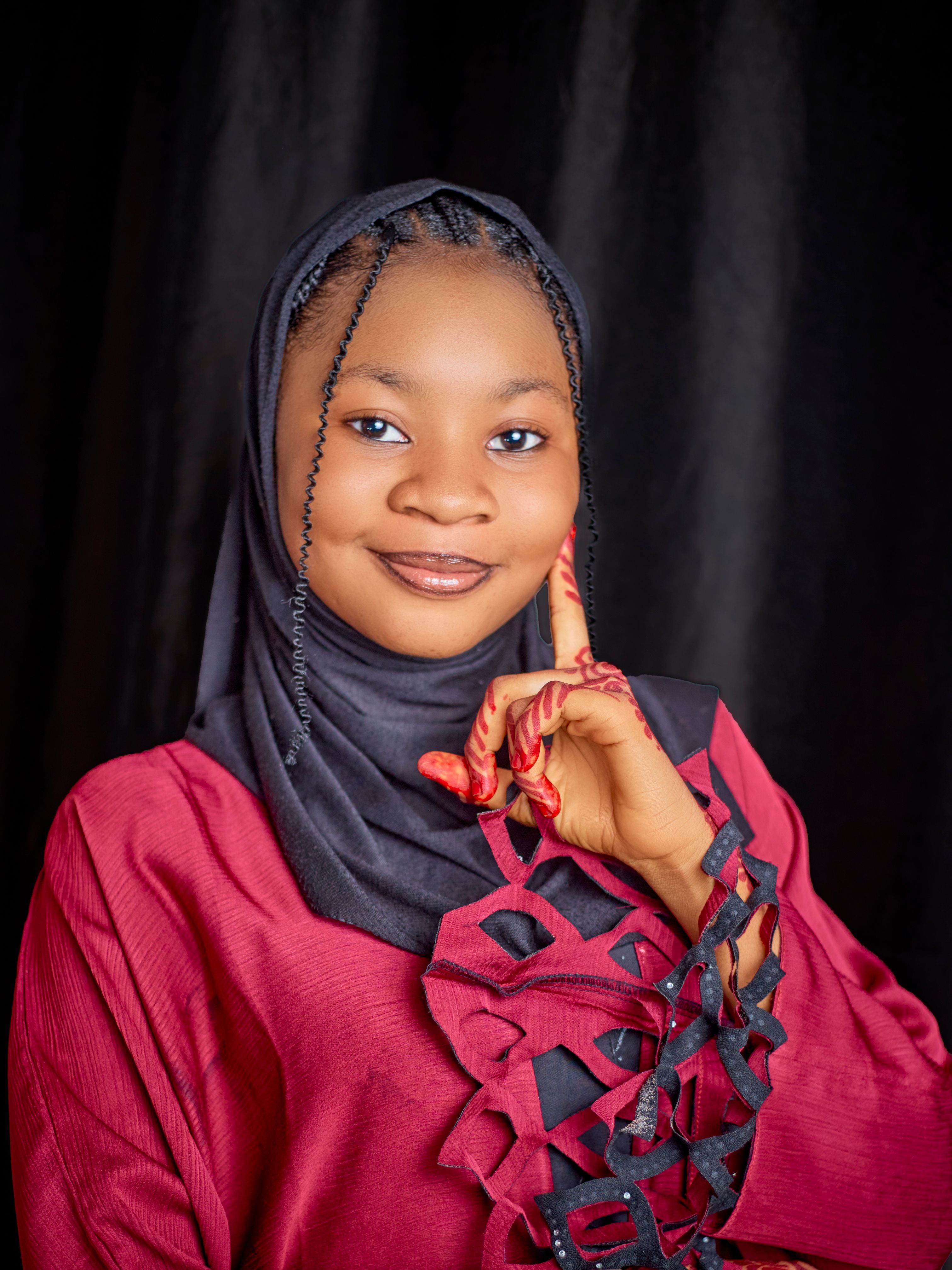 Portrait of a smiling young woman in a hijab with intricate henna designs, set against a black background.