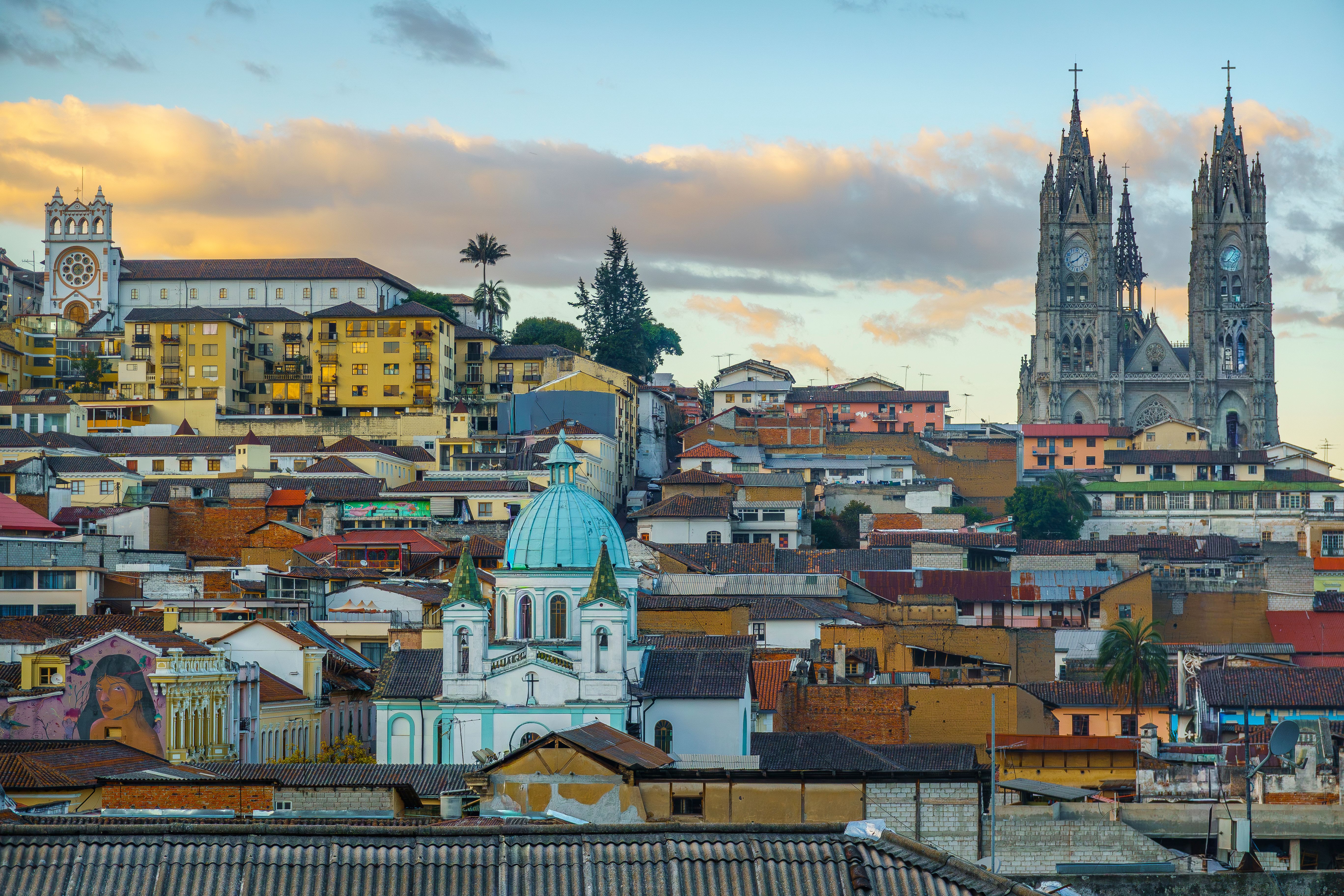A scenic view of Quito's historic skyline with iconic churches and colorful architecture at sunset.