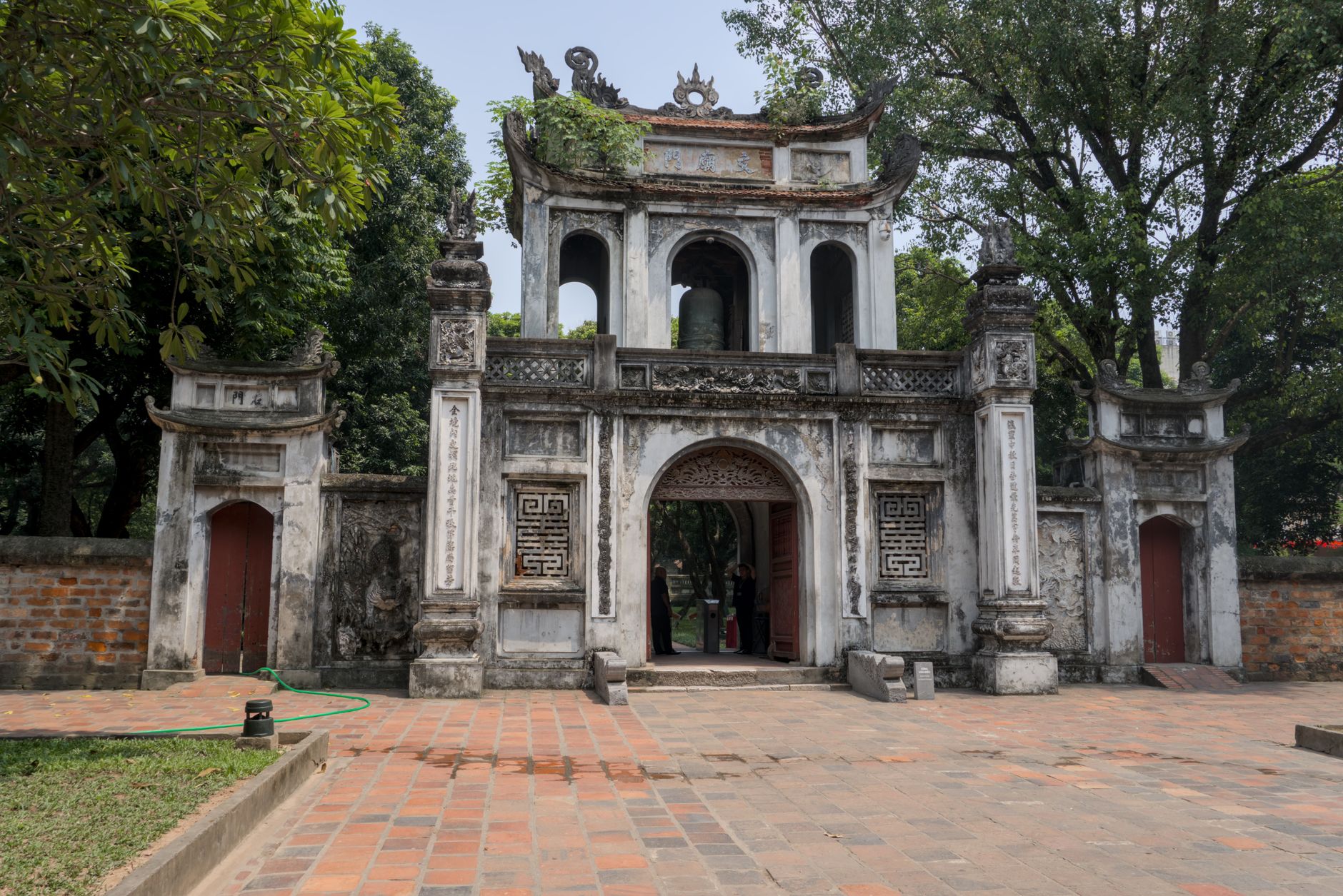 Historic temple entrance in Hanoi surrounded by lush greenery, evoking a serene atmosphere.