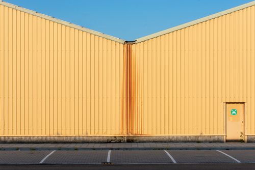 Free Symmetrical yellow industrial building facade with clear blue sky and parking lot. Stock Photo