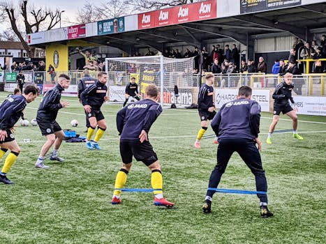 Players performing warmup exercises on a football field in England with spectators watching.
