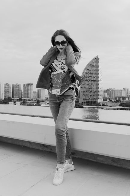 Trendy woman in sunglasses poses on a rooftop with Baku skyline in the background.