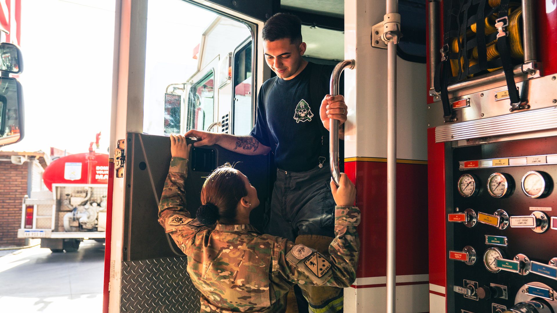 A firefighter and military personnel in uniform engage in casual conversation on a fire truck.