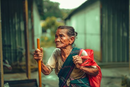 Free Portrait of an elderly woman with a walking stick and bag, captured outdoors. Stock Photo