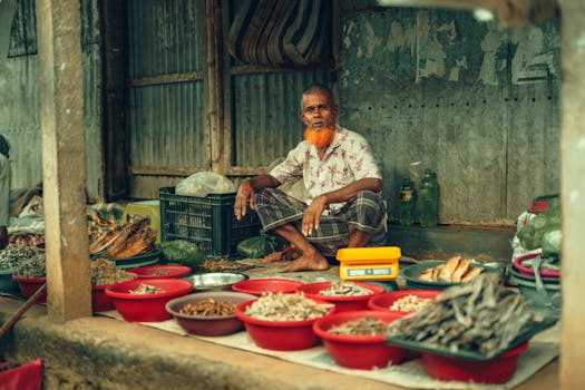 Elderly vendor selling dried goods at a vibrant street market in Bangladesh.