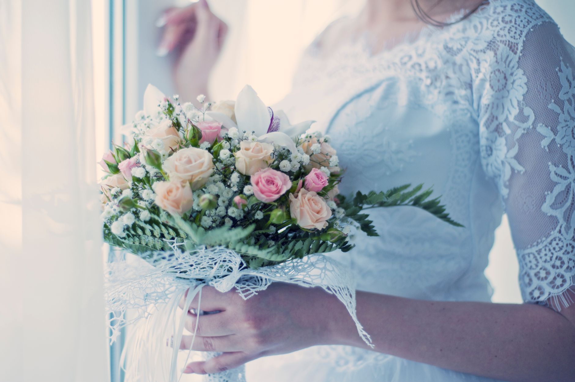 A bride in a lace dress holds an elegant bouquet of roses, embodying romance and purity.