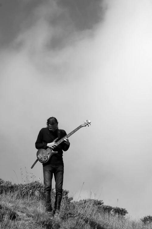 Free A musician plays bass guitar on a grassy hill under a cloudy sky in Qazvin Province, Iran. Stock Photo