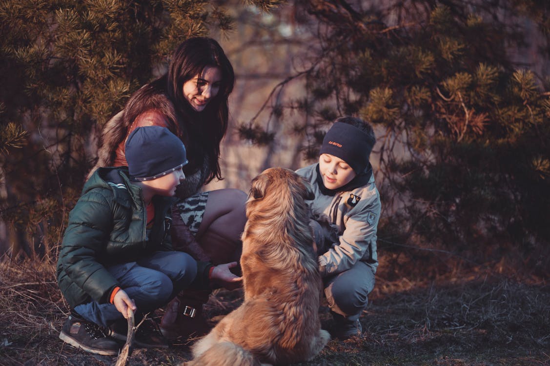 Three People Crouching in Front of Sitting Dog