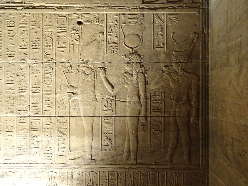 Intricate carvings of Egyptian deities and hieroglyphs on a temple wall, showcasing ancient art and history.