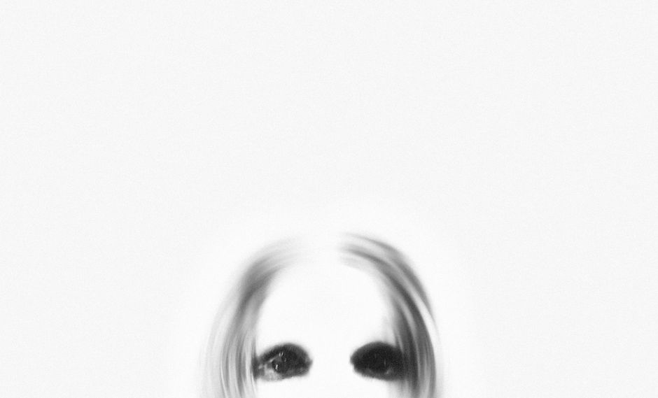 A ghostly figure with black eyes emerges from a blurred white background, creating a spooky atmosphere.