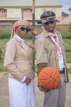 Stylish adults posing with a basketball, showcasing fashion and confidence outdoors.