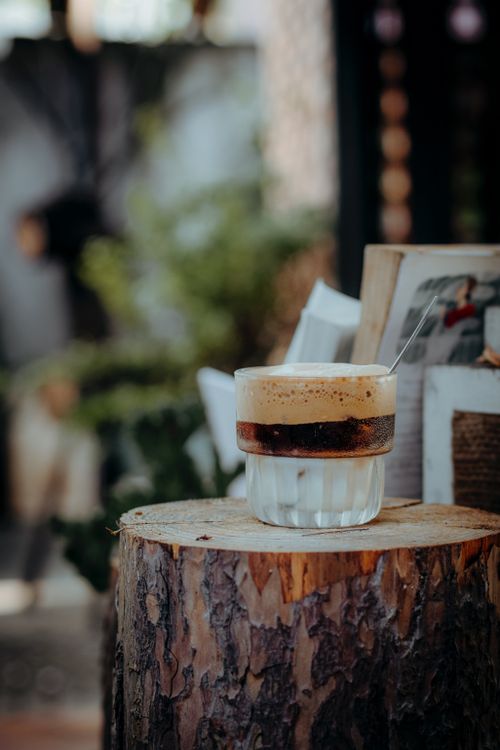Free A frothy coffee sits on a tree stump table in an outdoor setting, exuding rustic charm. Stock Photo