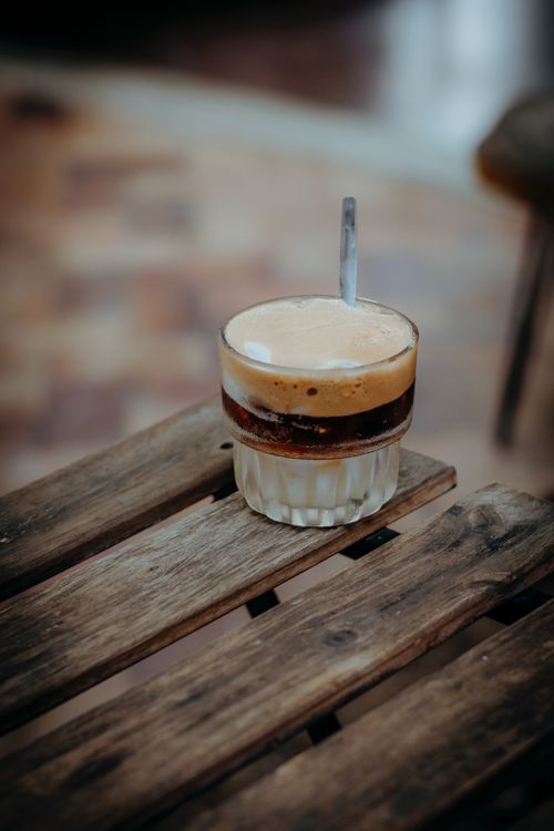 Free A glass of layered iced coffee sits on a rustic outdoor table, creating a cozy cafe vibe. Stock Photo
