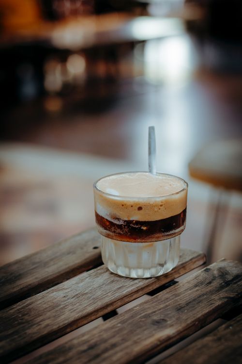 Free A close-up of a frothy iced coffee on a wooden table in a cozy cafe. Stock Photo