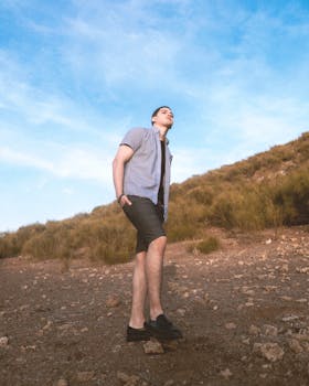 Young man standing confidently on a rocky hillside under a clear blue sky, exuding freedom and adventure.