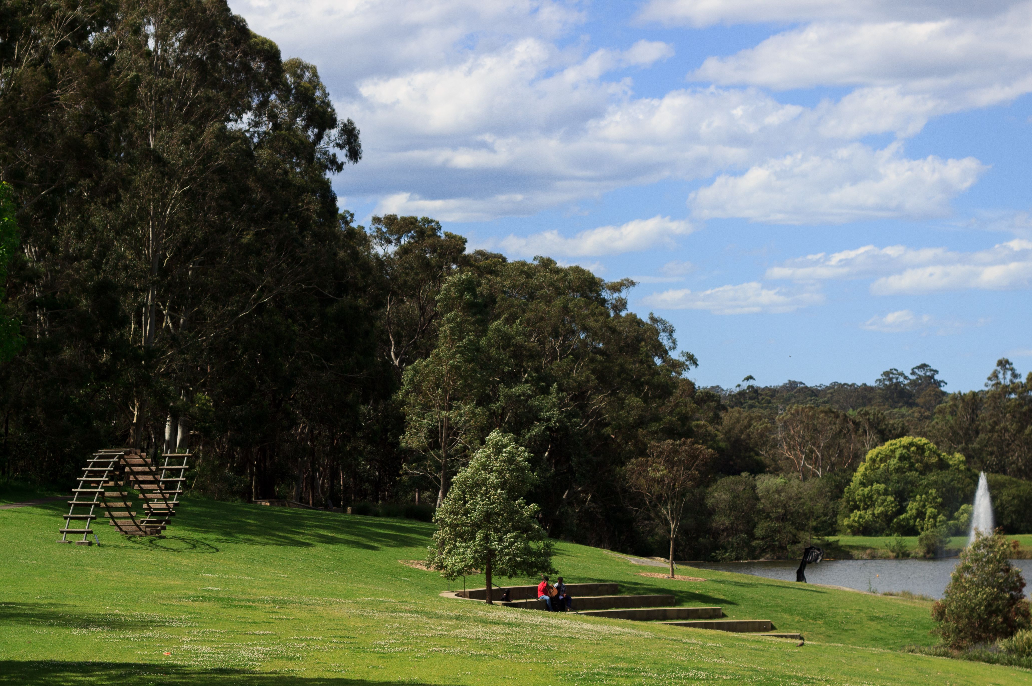 Idyllic park scene with sculpture, lake, and people relaxing on a sunny day.