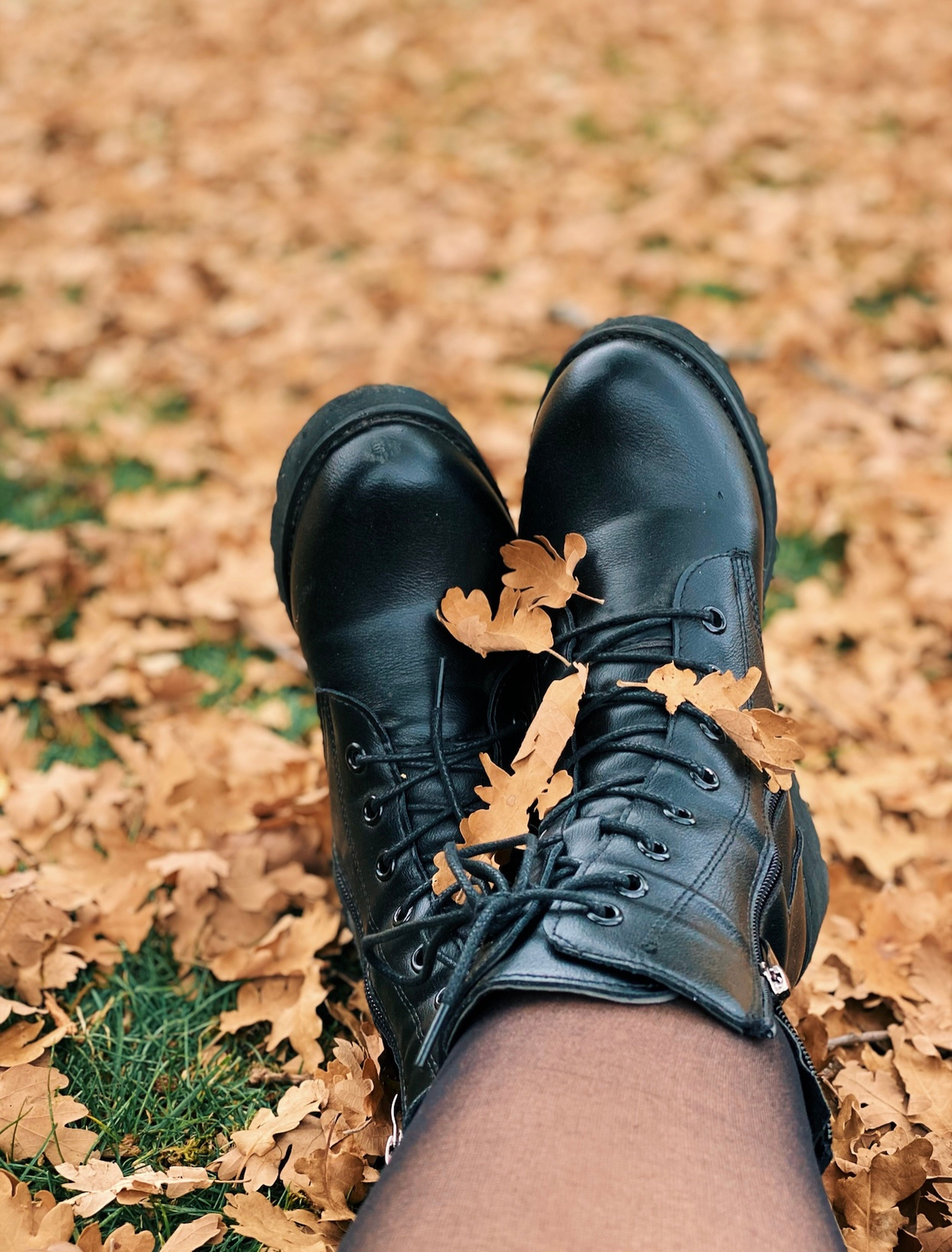Black leather boots on autumn leaves, perfect for a cozy fall vibe.
