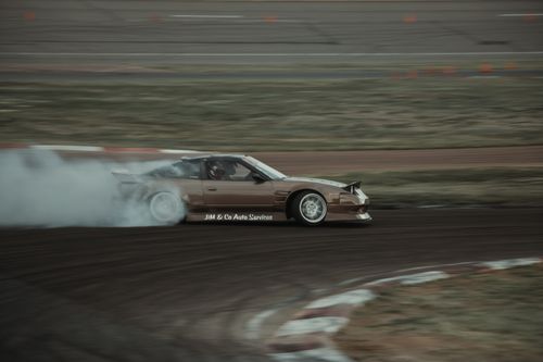 Free Brown Nissan drifting on a race track in Colorado Springs, creating a dynamic motion blur effect. Stock Photo