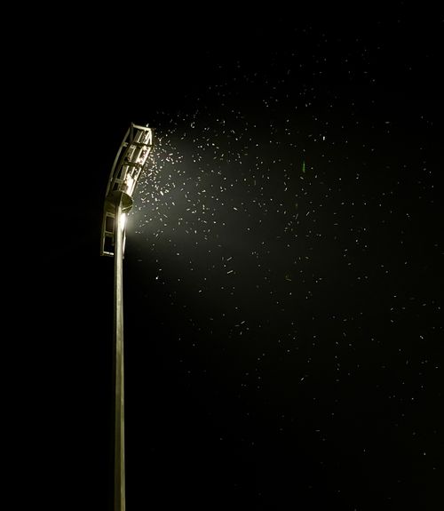 Free A high floodlight illuminating insects in the night sky, creating a dramatic scene. Stock Photo
