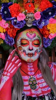 Colorful Dia de los Muertos face paint with floral headpiece and skull decorations.