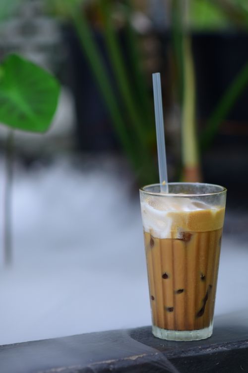 Free A glass of iced coffee with cream on an outdoor table, surrounded by greenery. Stock Photo