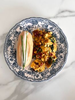 Delicious scrambled eggs with sun-dried tomatoes and a baguette on a vintage plate.