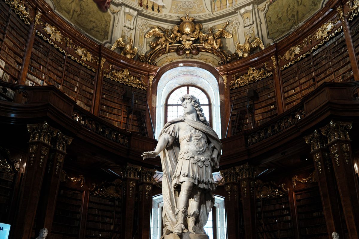Rafturi baroce pe doua niveluri si o statuie intr-o sala de biblioteca