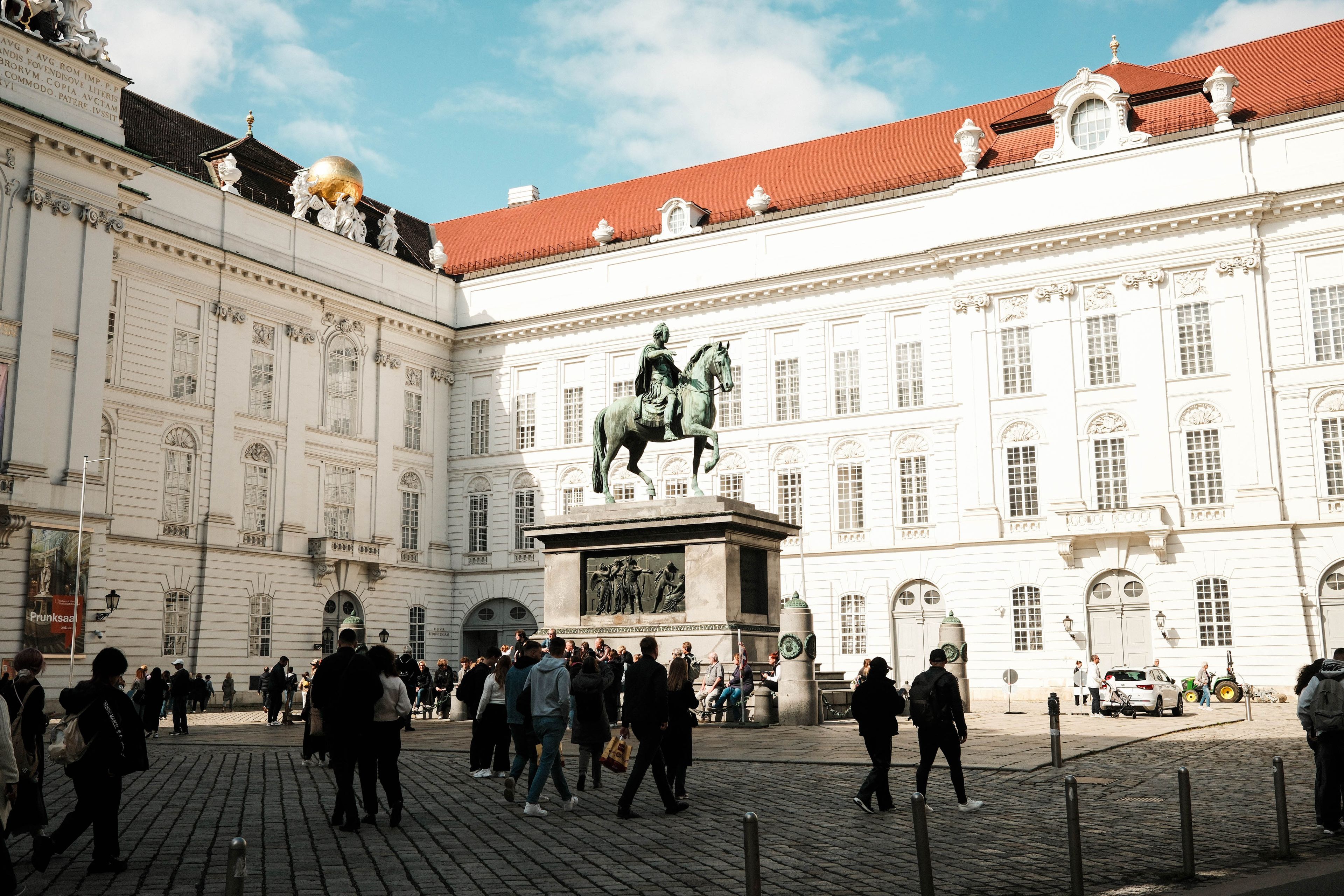 Tourists explore the Hofburg Palace courtyard in Vienna, highlighting its historic architecture and statue.