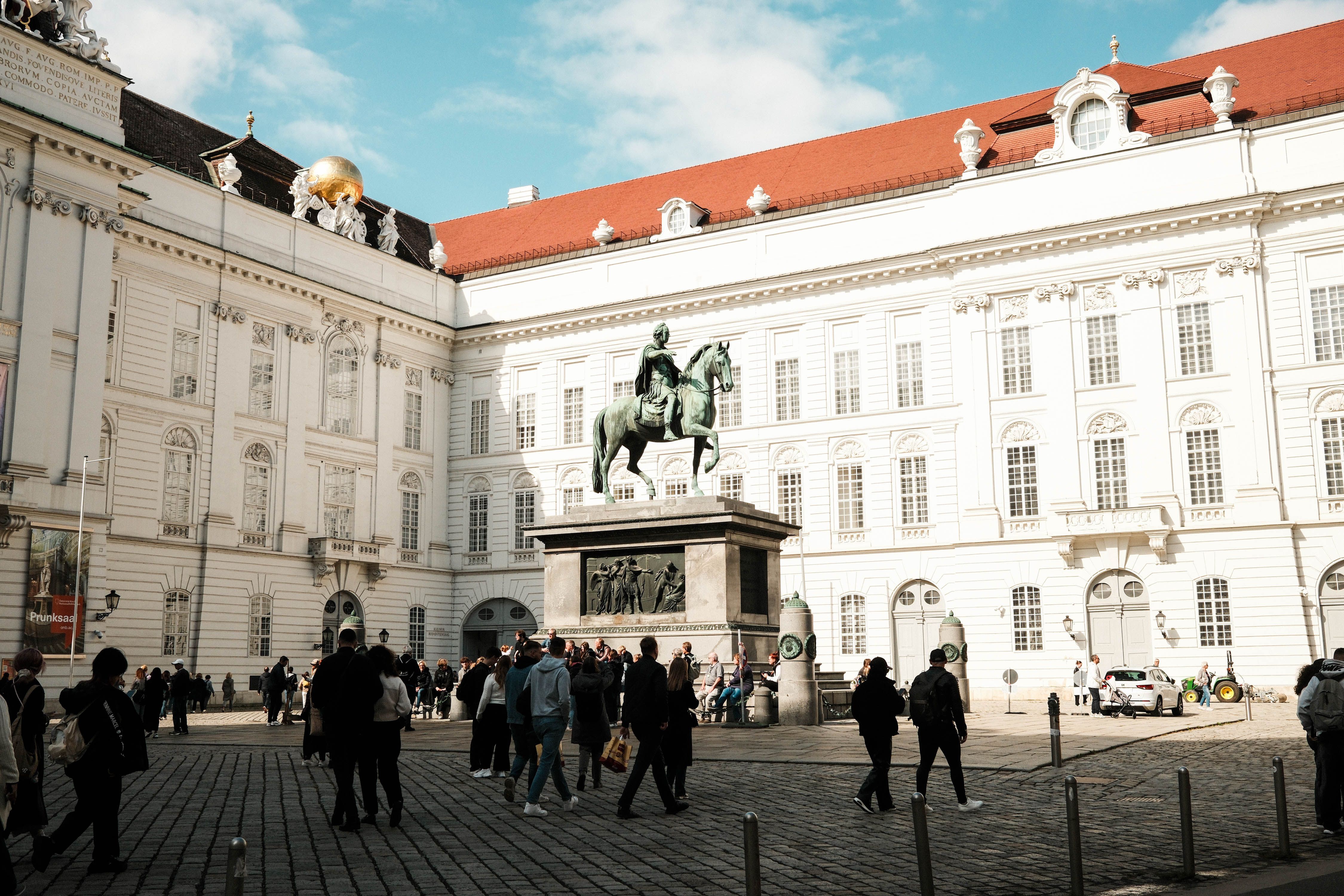 Courtyard scene at Hofburg, Vienna, Austria, with tourists, cobblestones, and an equestrian statue framed by palace wings.