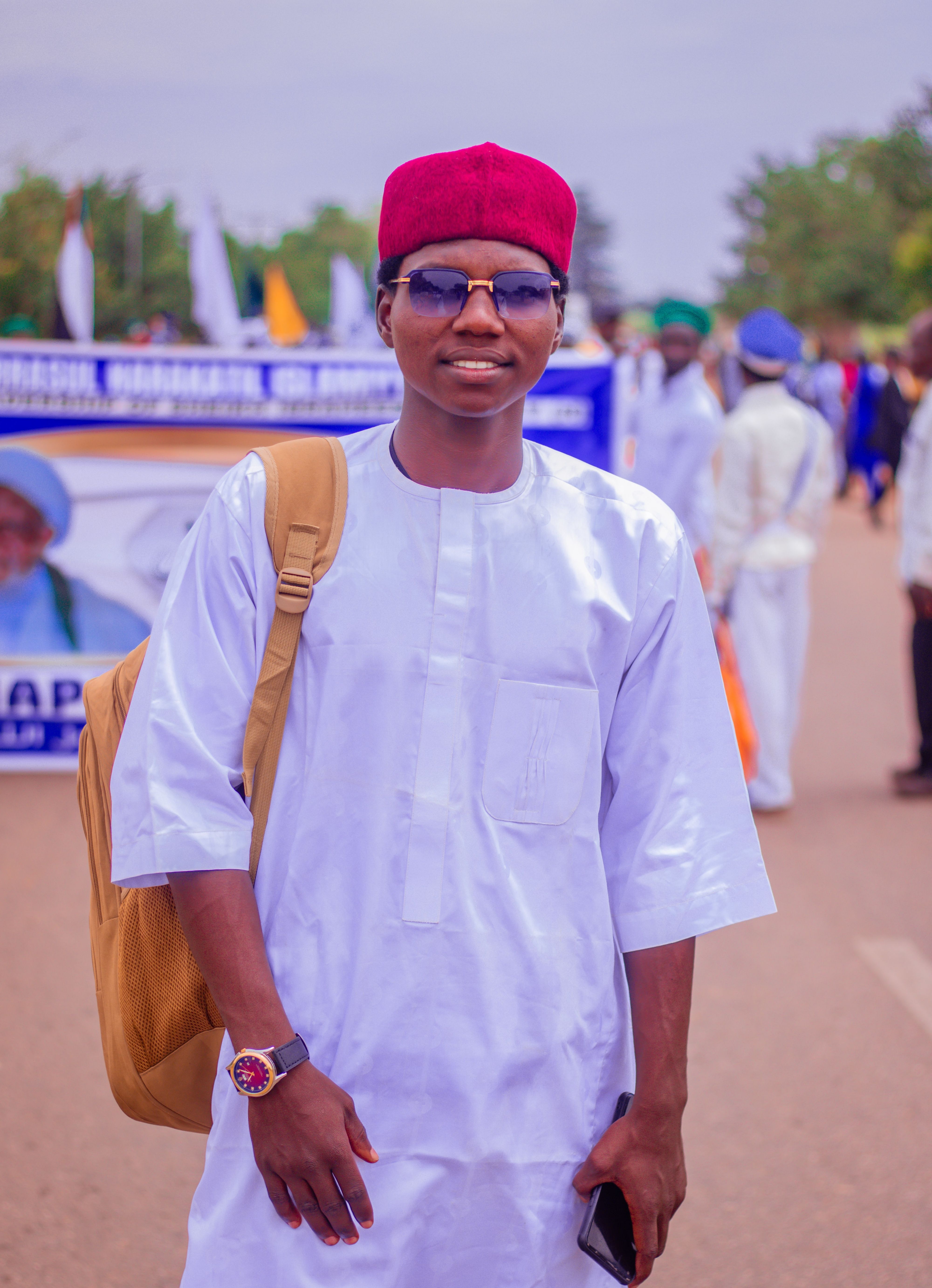 Portrait of a young man wearing traditional clothing and red cap at an outdoor event.