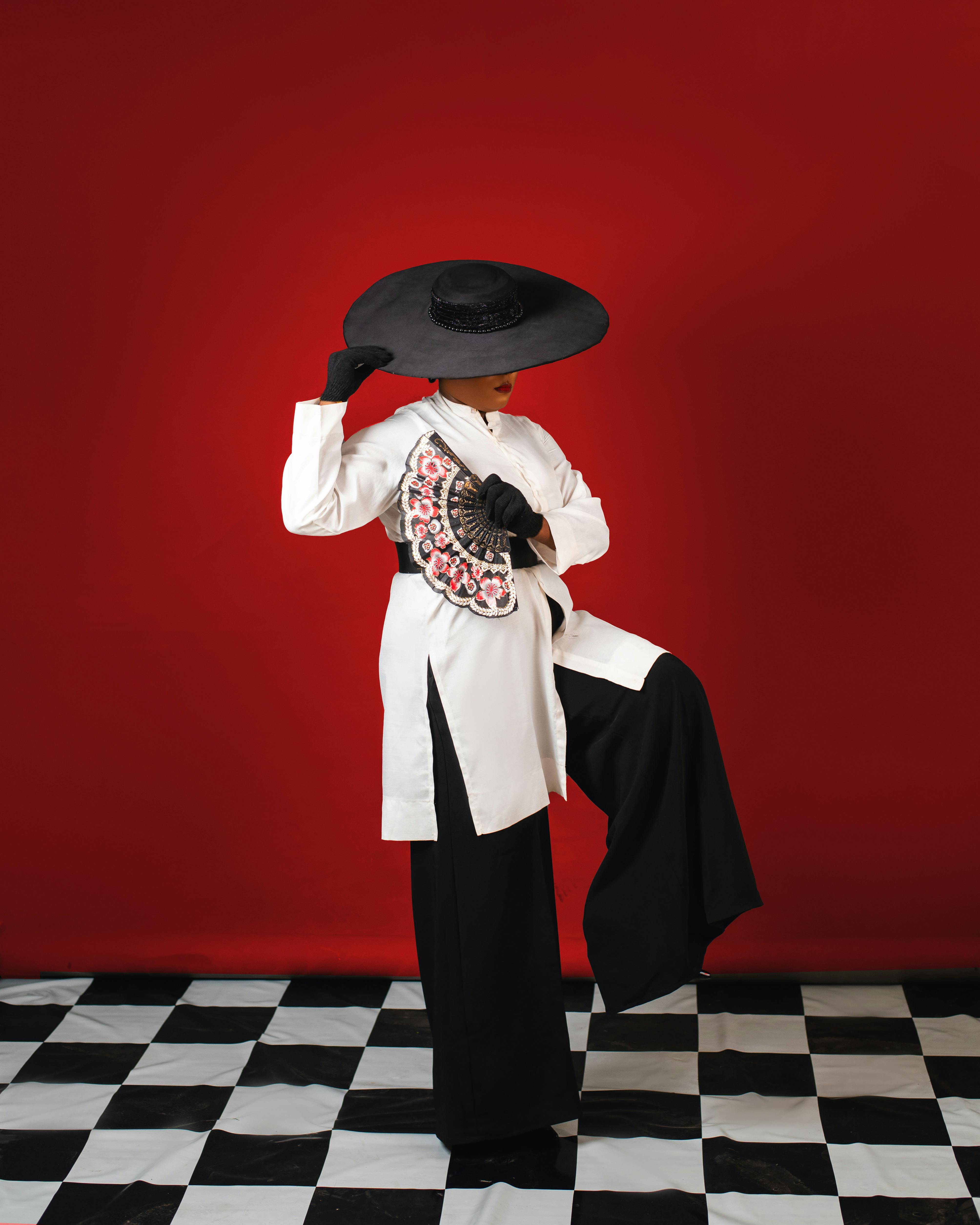 Chic portrait of a person with a fan and hat on checkered floor, red background