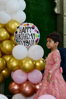 Adorable child in traditional dress at a vibrant birthday celebration with balloons.