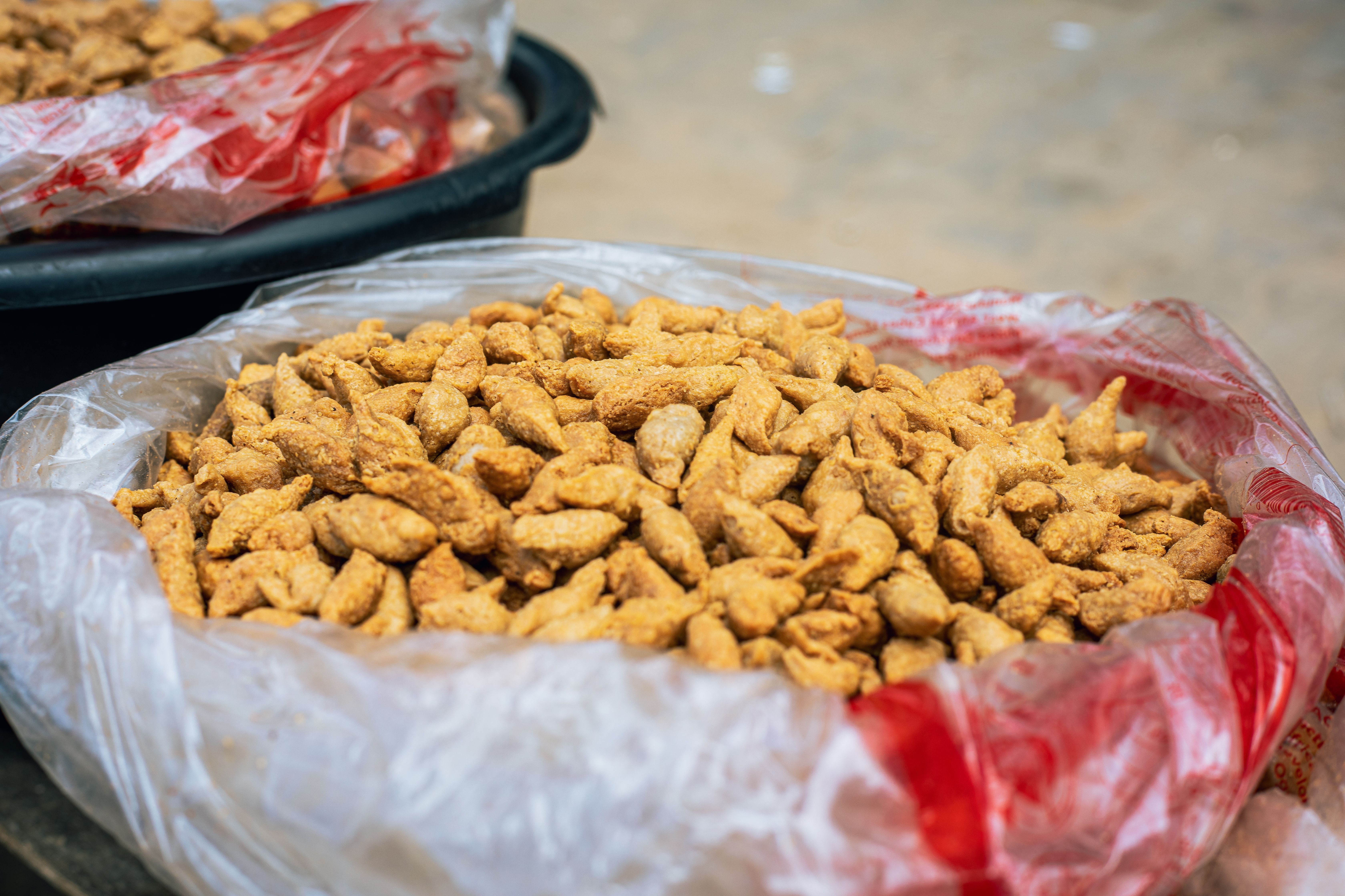 Close-up of crispy fried snacks in plastic bag at outdoor market.