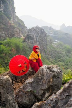 Woman in colorful dress with red umbrella on rocky mountain landscape in Jawa Barat, Indonesia.