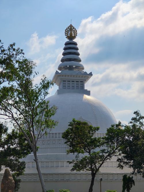 Free Beautiful view of a white Buddhist stupa surrounded by lush greenery under a bright blue sky. Stock Photo