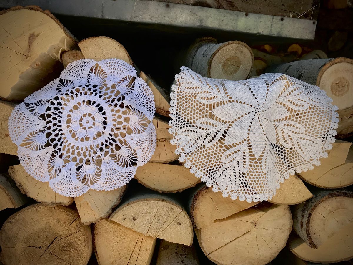 Beautiful crochet doilies displayed on stack of firewood, showcasing craftsmanship.