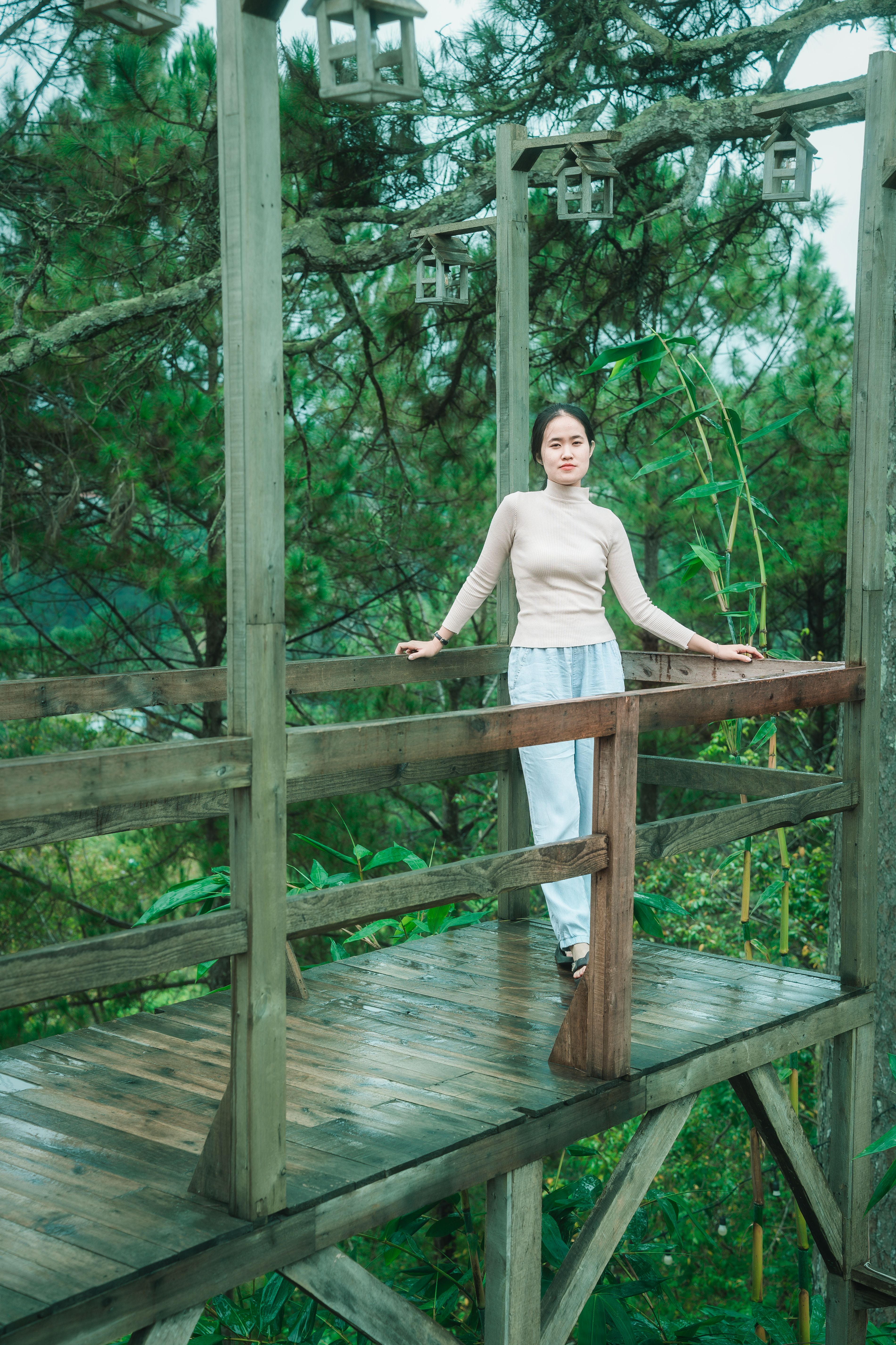 Woman standing on a wooden structure surrounded by lush greenery, evoking a serene natural vibe.